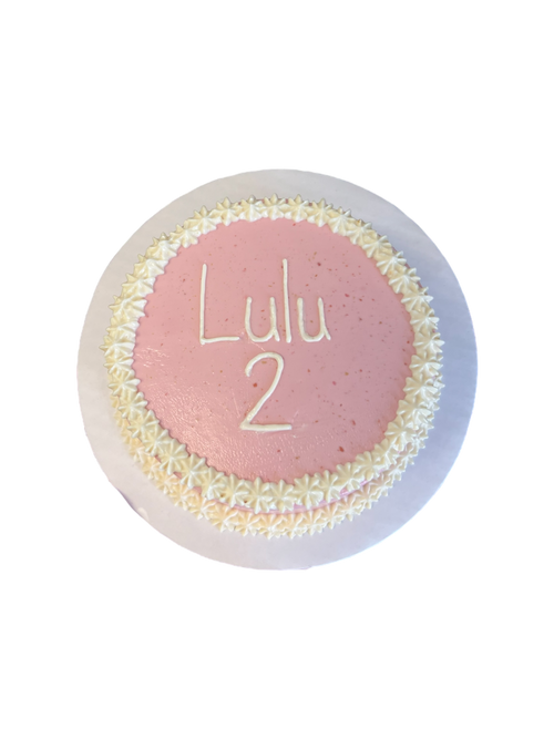 Circle dog birthday cake decorated with pink icing and white flower accents for pet celebrations
