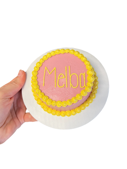 Circle dog birthday cake decorated with pink frosting and yellow floral edges for celebrating pets