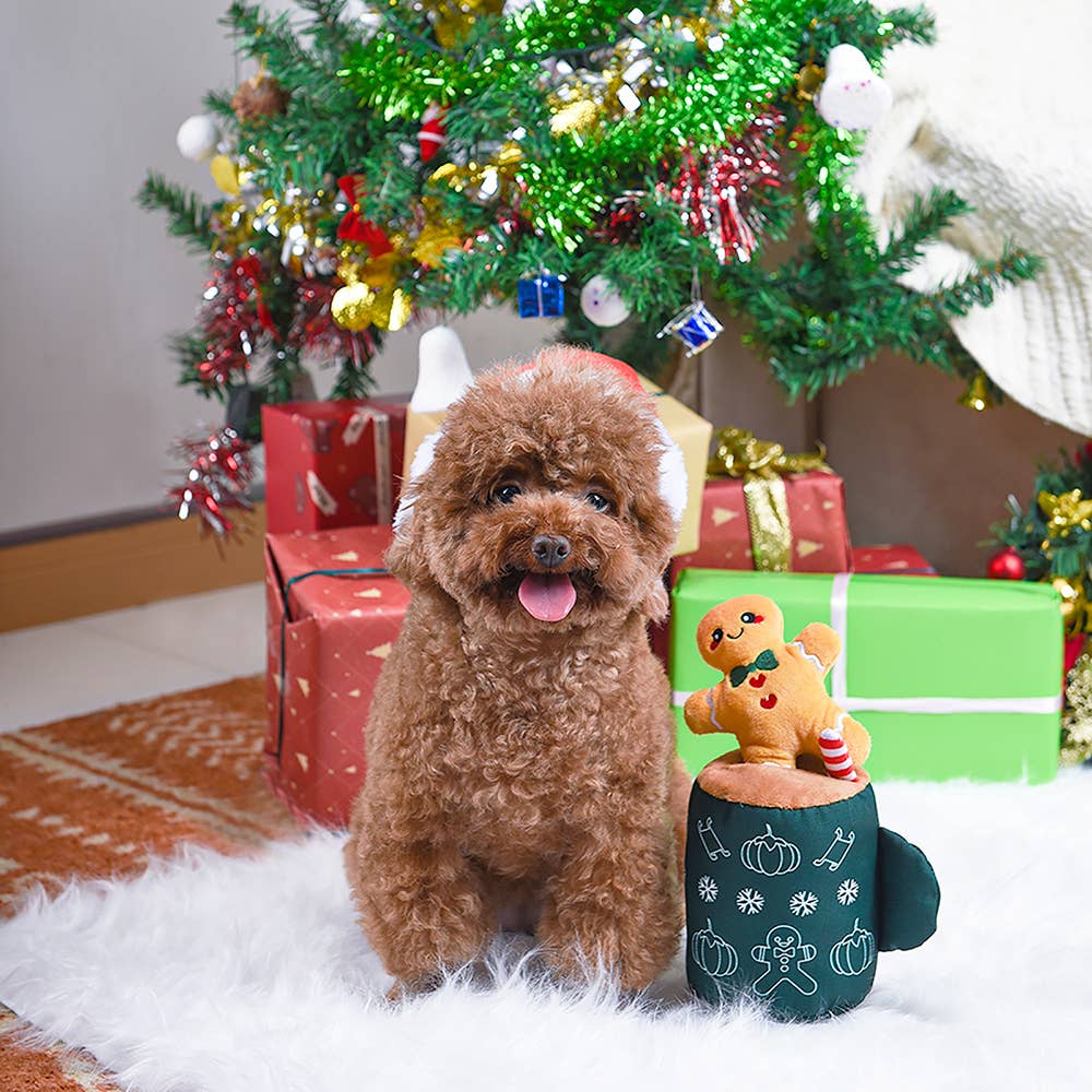 Cute dog sits beside gingerbread latte dog toy with festive holiday decorations in the background